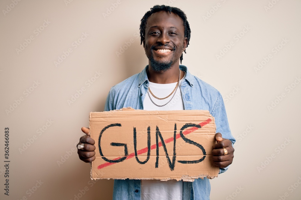 Young african american man asking for peace holding banner with prohibited guns message with a happy face standing and smiling with a confident smile showing teeth