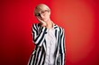 © Krakenimages.com - Blonde business woman with short hair wearing glasses and striped jacket over red background thinking looking tired and bored with depression problems with crossed arms.