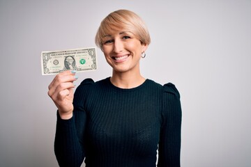 Poster - Young blonde woman with short hair holding one dollar banknote over isolated background with a happy face standing and smiling with a confident smile showing teeth