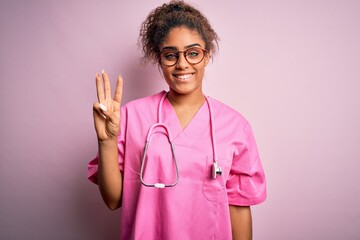 Poster - African american nurse girl wearing medical uniform and stethoscope over pink background showing and pointing up with fingers number three while smiling confident and happy.