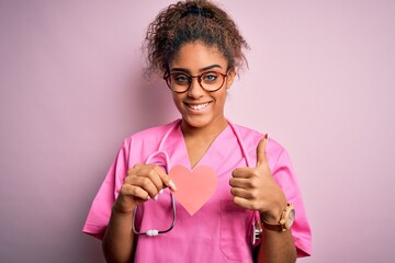 Poster - African american cardiologist girl wearing medical uniform and stethoscope holding heart happy with big smile doing ok sign, thumb up with fingers, excellent sign