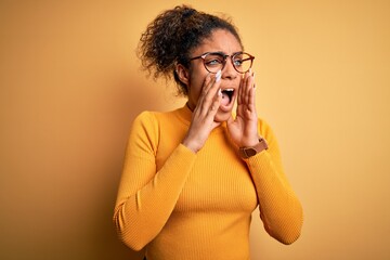 Sticker - Young beautiful african american girl wearing sweater and glasses over yellow background Shouting angry out loud with hands over mouth