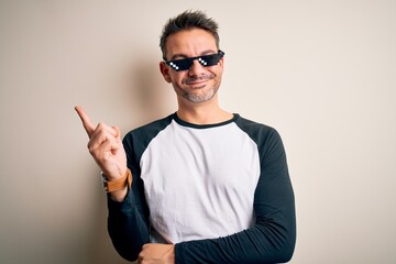 Young handsome man wearing funny thug life sunglasses meme over white background with a big smile on face, pointing with hand and finger to the side looking at the camera.