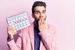 © Krakenimages.com - Young handsome man with beard holding calendar with hearts covering mouth with hand, shocked and afraid for mistake. surprised expression