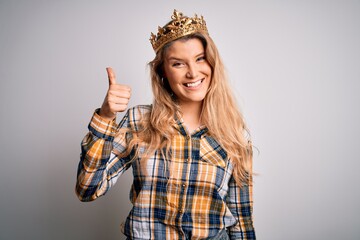 Canvas Print - Young beautiful blonde woman wearing golden crown of queen over isolated white background doing happy thumbs up gesture with hand. Approving expression looking at the camera showing success.