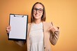 © Krakenimages.com - Beautiful inspector woman wearing glasses holding checklist clipboard over yellow background with surprise face pointing finger to himself