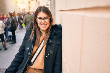 Canvas Print - Young beautiful brunette woman wearing glasses smiling happy and confident. Standing with smile on face leaning on the wall at street of city