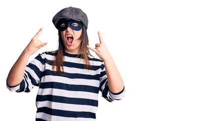 Canvas Print - Young beautiful brunette woman wearing burglar mask shouting with crazy expression doing rock symbol with hands up. music star. heavy concept.