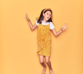 Adorable hispanic child girl wearing casual dress and diadem smiling happy. Jumping with smile on face over isolated yellow background