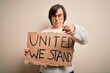 © Krakenimages.com - Young down syndrome woman holding protest banner with united we stand rights message pointing with finger to the camera and to you, hand sign, positive and confident gesture from the front