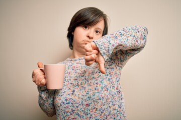 Sticker - Young down syndrome woman drinking a cup of hot coffee over isolated background with angry face, negative sign showing dislike with thumbs down, rejection concept