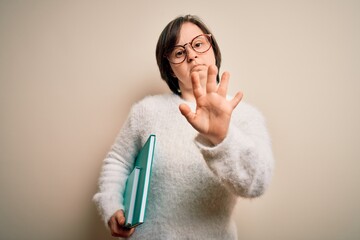 Poster - Young down syndrome student woman reading a book from library over isolated background with open hand doing stop sign with serious and confident expression, defense gesture