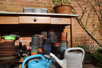 Wood potting bench work table with galvanized metal top. Used plastic empty plant pots, saucers and two watering cans in the sun towards the end of the winter in the Netherlands. February 23, 2020.  