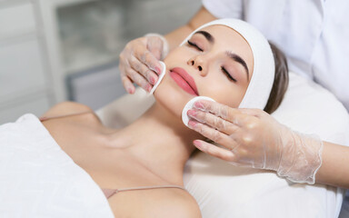 close up of beautician hands doing facial cleansing of a young woman using cotton pads or sponge in 