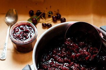 Cooked homemade cherry jam in the bowl and in the jar, raw cherries near on the table, organic meal and dessert concept