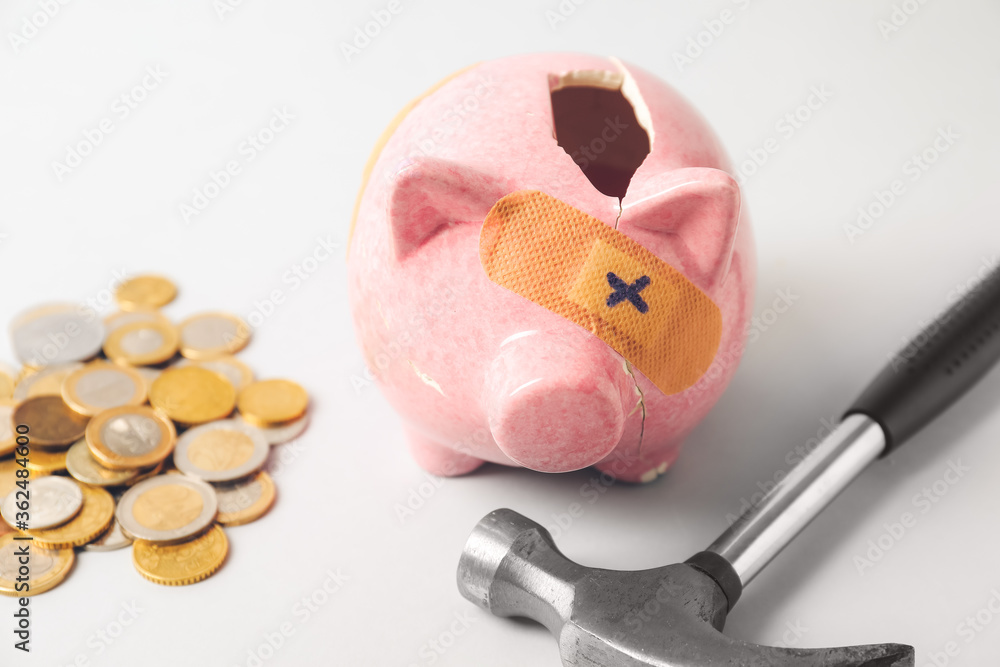 Broken patched piggy bank, hammer and money on light background