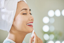Happy Young Asian Woman Enjoying Applying Refreshing Soothing Treatment Lotion On Her Face With Cotton Pad