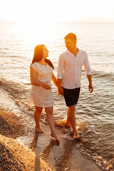 Wall Mural - Loving couple in white clothes during a honeymoon at sea walk on the sand at a photoshoot Love Story, ocean coast, beach