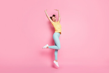 Wall Mural - Full body profile photo of attractive lady two buns hold arms up jumping high rejoicing carefree good mood wear casual striped t-shirt pants shoes isolated pink color background