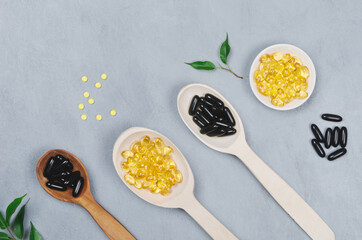 Black and yellow pills on wooden spoon on gray background