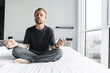 © Drobot Dean - Photo of pleased man meditating with eyes closed while sitting on bed