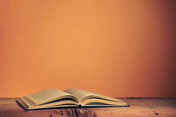 Poster - Beautiful ancient open old book on a red  wooden table and orange wall background behind.