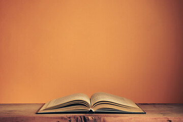 Poster - Beautiful ancient open old book on a red  wooden table and orange wall background behind.
