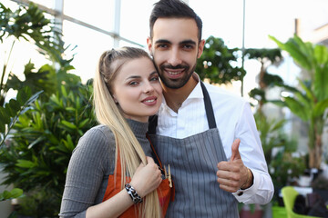 Portrait of positive man and woman working together in glasshouse and looking at camera