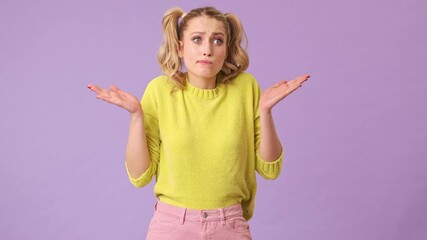 Poster - A gorgeous blonde girl in a yellow sweater does not know what to do, spread her arms to the sides in an isolated studio on a purple background