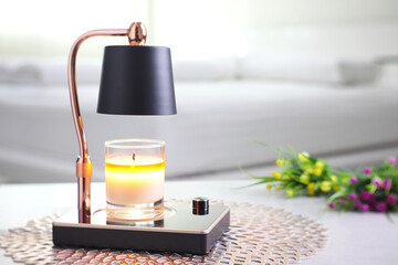 The luxury lighting aromatic scent  glass candle is put on the electric lamp candle warmer heater on the grey table in the white bedroom to create relax and romantic ambient