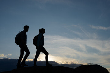 Wall Mural - Young Happy Travelers Hiking with Backpacks on the Rocky Trail at Summer Sunset. Family Travel and Adventure Concept.