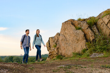 Wall Mural - young happy travelers hiking with backpacks on the rocky trail at summer sunset. family travel and a