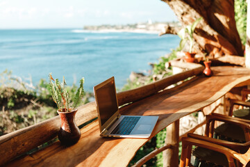 Open laptop with black screen  on wooden table work space outdoors with amazing view on the ocean. Laptop on sea view backdrop