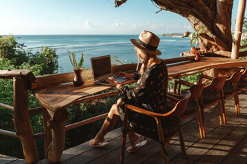 freelance concept. pretty young woman using laptop in cafe on tropical beach in outdoor cafe terrace