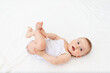 © Any Grant - baby girl 6 months old lying in a crib in the children's room on her back and holding her legs, looking at the camera, baby's morning, baby products concept