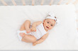 © Any Grant - baby girl 6 months old lies in a crib in the nursery with white clothes on her back and laughs, looks at the camera, baby's morning, baby products concept