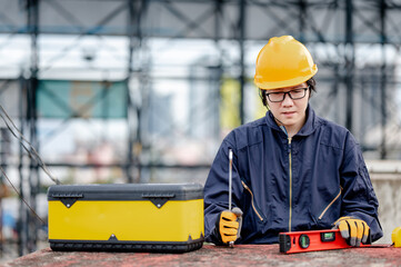 Male Asian mechanic or maintenance worker man wearing protective suit and helmet holding wrench and level tool near work tool box at construction site. Equipment for mechanical engineering project