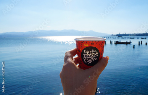 Close-up Of Human Hand With Coffee Cup Against Sea