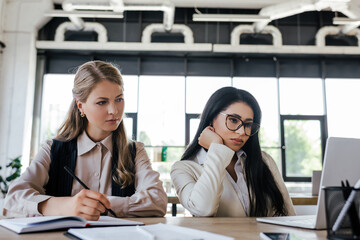 Poster - selective focus of bored businesswomen looking at laptop in office