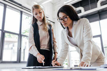 Poster - selective focus of attractive businesswoman in glasses signing contract near coworker with pen