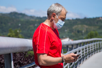 Wall Mural - mature man with medical mask on the street using the new phone in the new normal