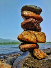 Stone Balancing of different sizes near a river with water flowing and mountains.