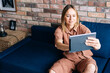 © dikushin - Young woman in casual clothes sitting on the couch with digital tablet computer and talking with her friends, remote communication. Concept of communication and coziness.