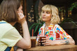 © Drobot Dean - Image of two women talking and drinking soda while sitting at table