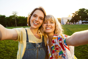 Sticker - Image of cheerful attractive two women taking selfie photo and hugging