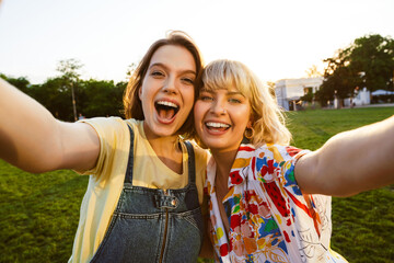 Sticker - Image of cheerful attractive two women taking selfie photo and hugging