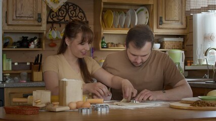 Wall Mural - Loving couple prepare cookies in the kitchen sitting at the table. They cook together in the kitchen and laugh. Happy family life. Cooking dough for baking. Flour products. Wooden kitchen.