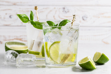 Refreshing iced drink with lime and basil on white wooden background close up. Tasty cold lemonade on the table.