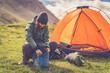 alpine woman folding sleeping bag and other accessories for camping. In the background orange tent and equipment for outdoor activities.