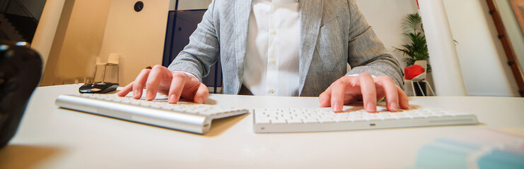 male programmer dressed in a gray jacket works with two keyboards on the table in the office